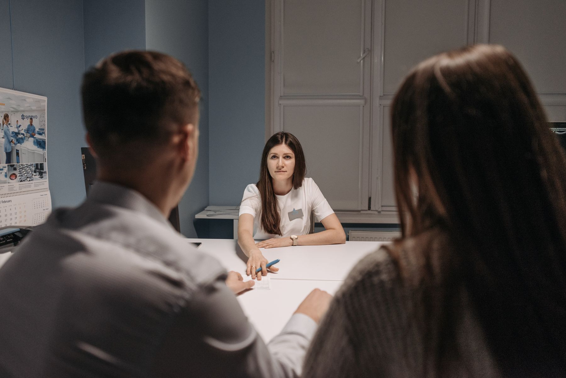 Site staff member speaking with two adults across a consultation table while intake information is organized.