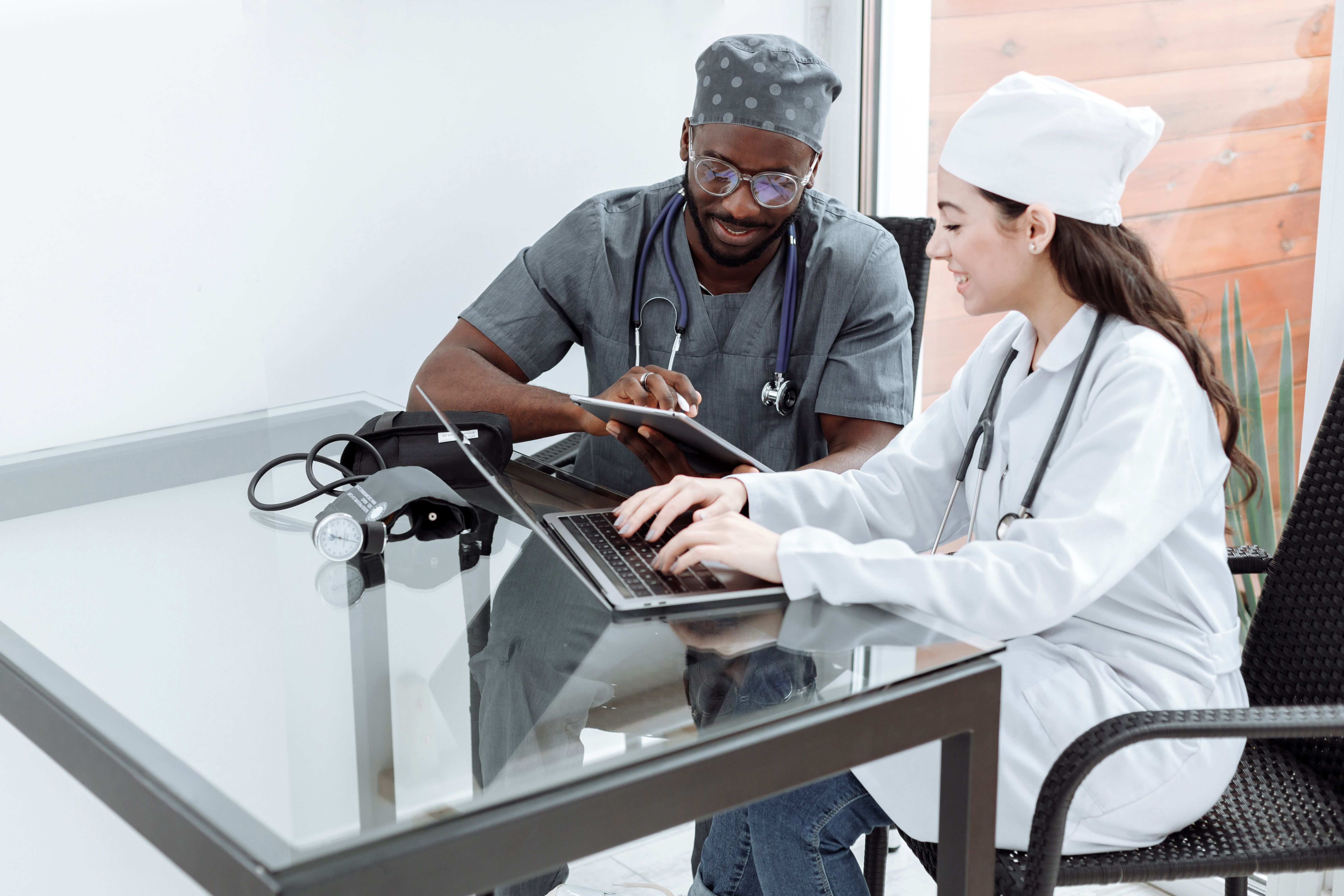 Two healthcare professionals reviewing information together with a laptop and tablet in a bright clinical office.